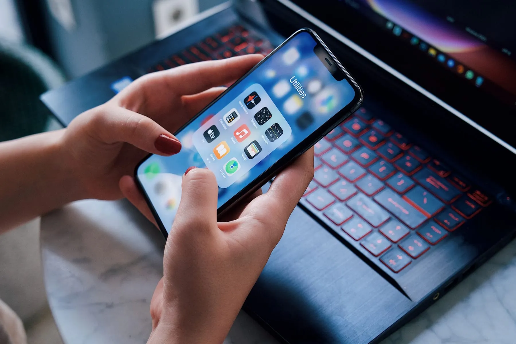Mãos segurando um smartphone com aplicativos abertos ao lado de um notebook