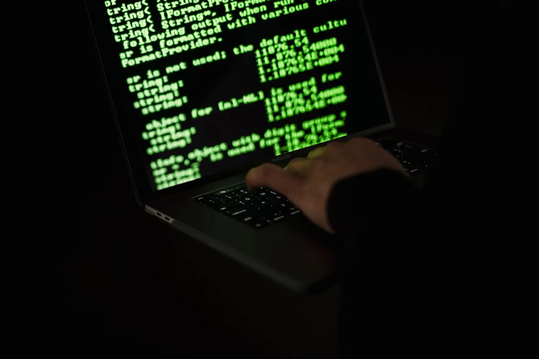 Pessoa digitando em um notebook com código verde na tela, no escuro
